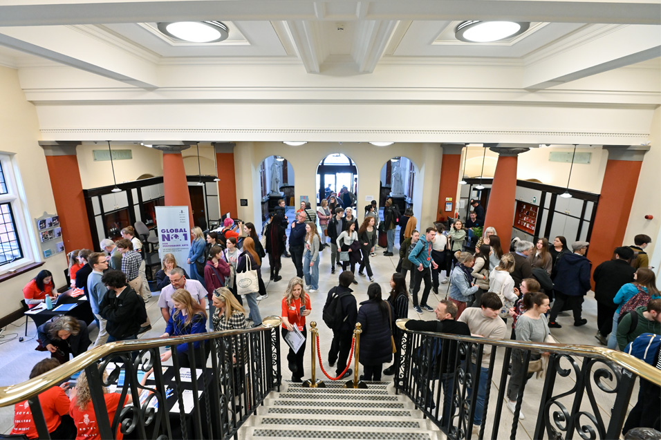 A group of people in a lobby area of a classically old building, with stairs leading up.